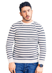 Fototapeta premium Young hispanic man wearing casual clothes in shock face, looking skeptical and sarcastic, surprised with open mouth