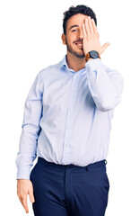 Young hispanic man wearing business clothes covering one eye with hand, confident smile on face and surprise emotion.