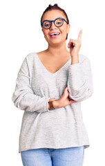 Young latin woman wearing casual clothes with a big smile on face, pointing with hand and finger to the side looking at the camera.