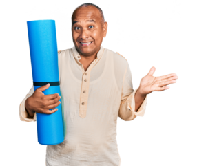 Hispanic middle age man holding yoga mat celebrating achievement with happy smile and winner expression with raised hand