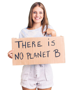 Young beautiful blonde woman holding there is no planet b banner pointing finger to one self smiling happy and proud
