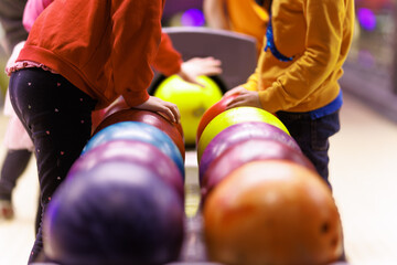 Children are playing bowling. Extracurricular activities for children. Bowling balls and bowling alley in the background - obrazy, fototapety, plakaty