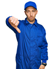 Bald man with beard wearing builder jumpsuit uniform looking unhappy and angry showing rejection and negative with thumbs down gesture. bad expression.