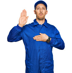 Bald man with beard wearing builder jumpsuit uniform swearing with hand on chest and open palm,...