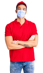 Young handsome hispanic man wearing delivery uniform and medical mask happy face smiling with crossed arms looking at the camera. positive person.