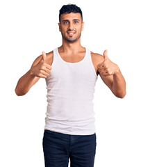 Naklejka premium Young hispanic man wearing casual clothes success sign doing positive gesture with hand, thumbs up smiling and happy. cheerful expression and winner gesture.