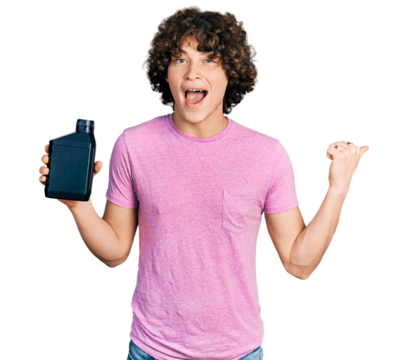 Caucasian teenager holding motor oil bottle pointing thumb up to the side smiling happy with open mouth
