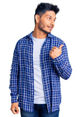 Handsome latin american young man wearing casual shirt smiling with happy face looking and pointing to the side with thumb up.