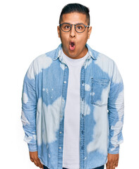 Young latin man wearing casual clothes and glasses scared and amazed with open mouth for surprise,...