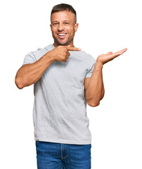 Handsome muscle man wearing casual grey tshirt amazed and smiling to the camera while presenting with hand and pointing with finger.