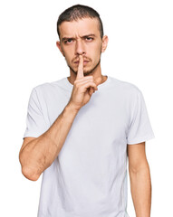 Hispanic young man wearing casual white t shirt asking to be quiet with finger on lips. silence and secret concept.