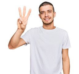 Naklejka premium Hispanic young man wearing casual white t shirt showing and pointing up with fingers number three while smiling confident and happy.