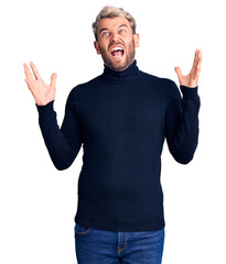 Fototapeta premium Young handsome blond man wearing casual turtleneck sweater crazy and mad shouting and yelling with aggressive expression and arms raised. frustration concept.