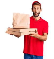 Handsome blond man with beard holding take away food scared and amazed with open mouth for...