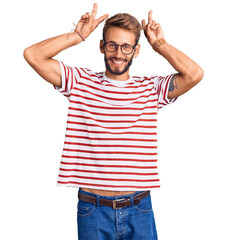 Handsome blond man with beard wearing casual clothes and glasses posing funny and crazy with fingers on head as bunny ears, smiling cheerful