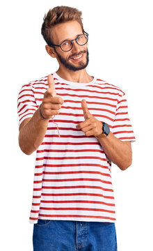Handsome blond man with beard wearing casual clothes and glasses pointing fingers to camera with happy and funny face. good energy and vibes.