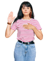 Young hispanic girl wearing casual clothes swearing with hand on chest and open palm, making a...