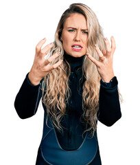Young blonde woman wearing diver neoprene uniform shouting frustrated with rage, hands trying to...