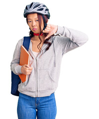 Young beautiful chinese girl wearing student backpack and bike helmet holding book with angry face, negative sign showing dislike with thumbs down, rejection concept