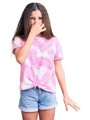 Cute hispanic child girl wearing casual clothes smelling something stinky and disgusting, intolerable smell, holding breath with fingers on nose. bad smell