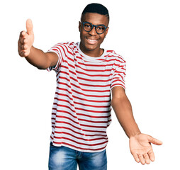 Young african american man wearing casual t shirt and glasses looking at the camera smiling with open arms for hug. cheerful expression embracing happiness.