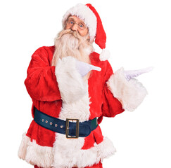 Old senior man with grey hair and long beard wearing traditional santa claus costume amazed and smiling to the camera while presenting with hand and pointing with finger.