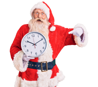 Old senior man with grey hair and long beard wearing santa claus costume holding clock smiling happy pointing with hand and finger