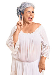 Senior woman with gray hair wearing bohemian style smiling with happy face winking at the camera doing victory sign with fingers. number two.