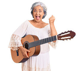 Senior woman with gray hair playing classical guitar screaming proud, celebrating victory and...