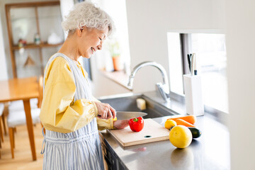 ひとり暮らしのシニア女性が自宅の台所で野菜を切っている/食事の支度