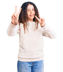 Beautiful kid girl with curly hair wearing casual clothes smiling looking to the camera showing fingers doing victory sign. number two.