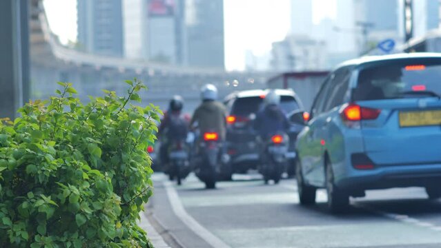Many motorcycles, cars, and taxis cross a plant on a modern city street in Jakarta. Depicts urban pollution and traffic density. Shot quite close up with a blurred background.