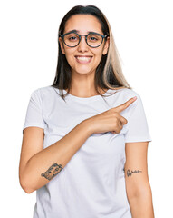 Young hispanic woman wearing casual white t shirt pointing aside worried and nervous with forefinger, concerned and surprised expression