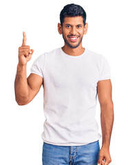 Fototapeta premium Young latin man wearing casual clothes showing and pointing up with finger number one while smiling confident and happy.