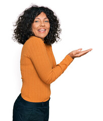 Young hispanic woman wearing casual clothes pointing aside with hands open palms showing copy space, presenting advertisement smiling excited happy