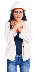 Young beautiful latin girl wearing architect hardhat and glasses shouting and suffocate because painful strangle. health problem. asphyxiate and suicide concept.