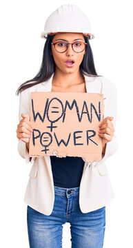 Young beautiful latin girl wearing architect hardhat holding woman power banner scared and amazed with open mouth for surprise, disbelief face