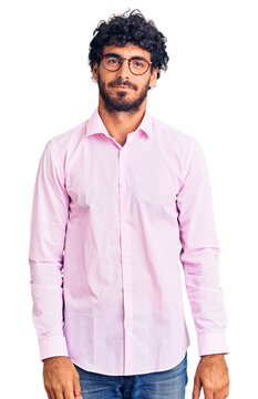 Handsome young man with curly hair and bear wearing business clothes relaxed with serious expression on face. simple and natural looking at the camera.