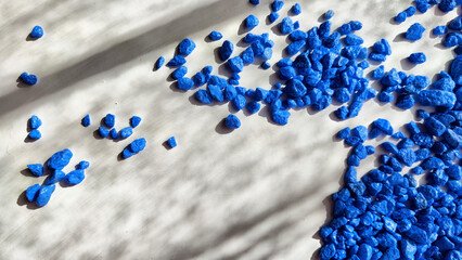 Fototapeta premium Blue painted small pebble on the surface of a table under sunlight. Abstract background, texture, frame, and copy space. Supplies for crafting and handmade.