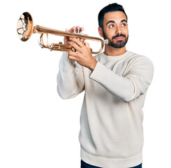 Young hispanic man with beard playing trumpet smiling looking to the side and staring away thinking.