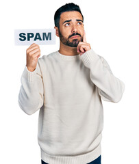 Young hispanic man with beard holding spam banner serious face thinking about question with hand on...