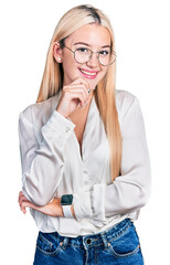 Beautiful blonde woman wearing elegant shirt and glasses looking confident at the camera smiling with crossed arms and hand raised on chin. thinking positive.