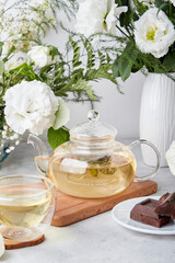 Obraz na płótnie Canvas Aesthetic tea time, teapot, green tea and chocolate in biophilic interior among white flowers. Feminine calm lifestyle, cozy home concept