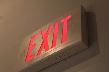 A lose up photo of a red exit sign high up on the wall. 