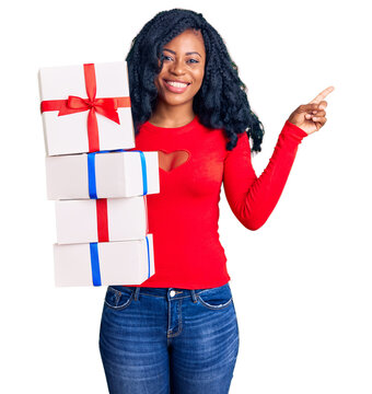 Beautiful african american woman holding presents smiling happy pointing with hand and finger to the side