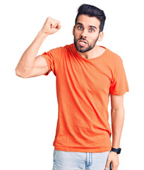 Young handsome man with beard wearing casual t-shirt angry and mad raising fist frustrated and furious while shouting with anger. rage and aggressive concept.