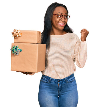 Young black woman holding gifts pointing thumb up to the side smiling happy with open mouth