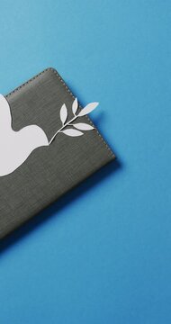 Vertical video of white dove with leaf on grey notebook and copy space on blue background