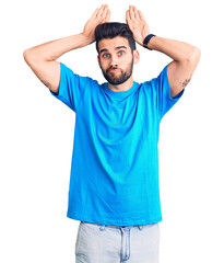 Fototapeta premium Young handsome man with beard wearing casual t-shirt doing bunny ears gesture with hands palms looking cynical and skeptical. easter rabbit concept.