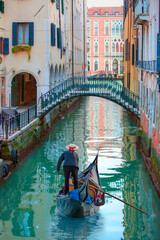 Fototapeta na wymiar Venetian gondolier punting gondola through green canal waters of Venice Italy